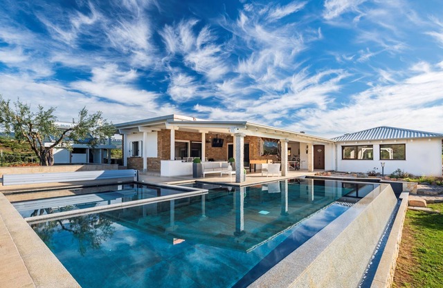 Villa con piscina climatizada rodeada de vegetación.